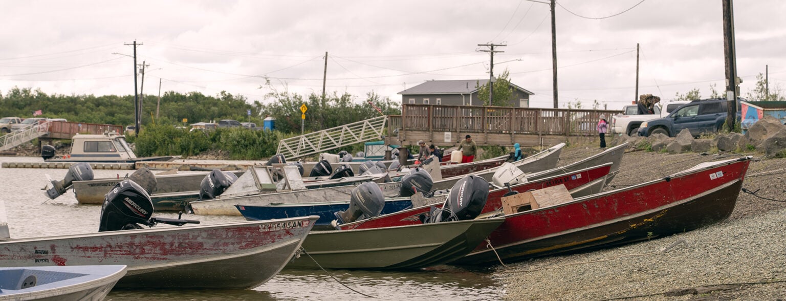 People stand among rows of motorboats along the waterfront in Bethel, Alaska.