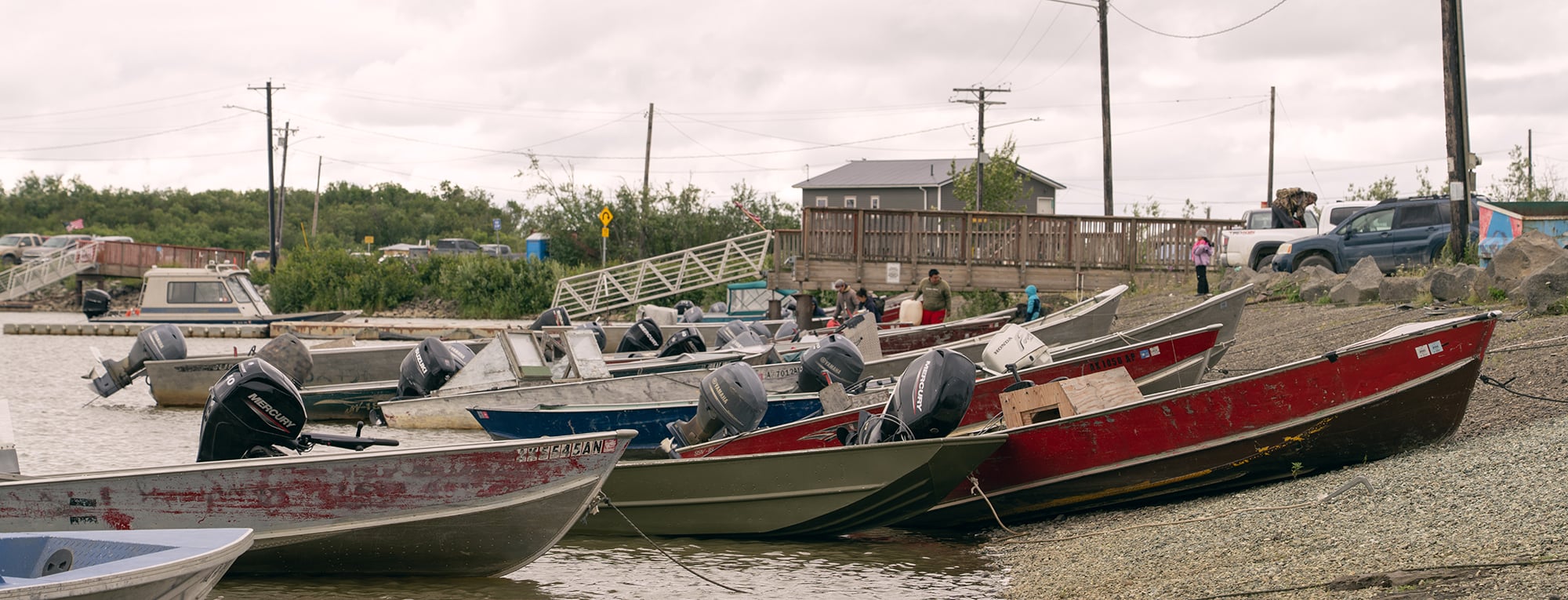 People stand among rows of motorboats along the waterfront in Bethel, Alaska.