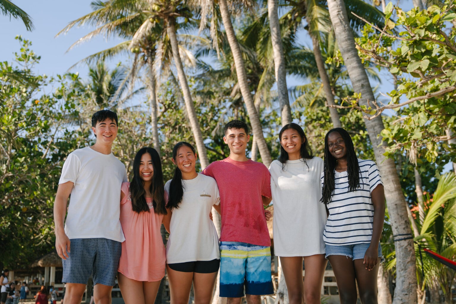 Young people in casual clothes standing in a tropical location in front of palm trees