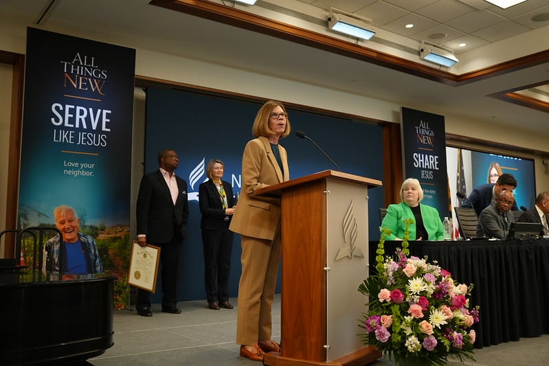 Woman in business suit stands on a stage and presents from a podium.