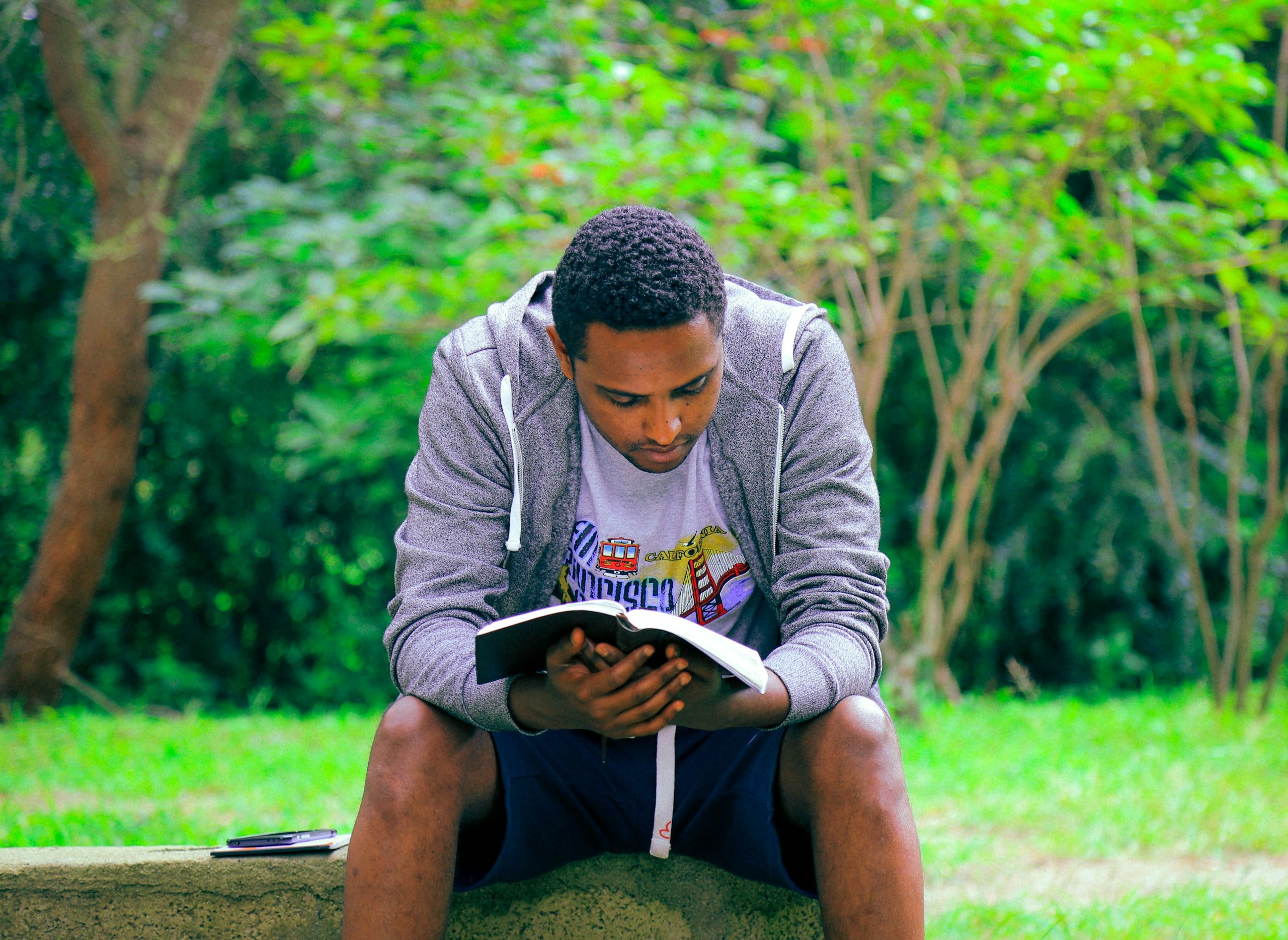 man sitting on concrete bench reading book