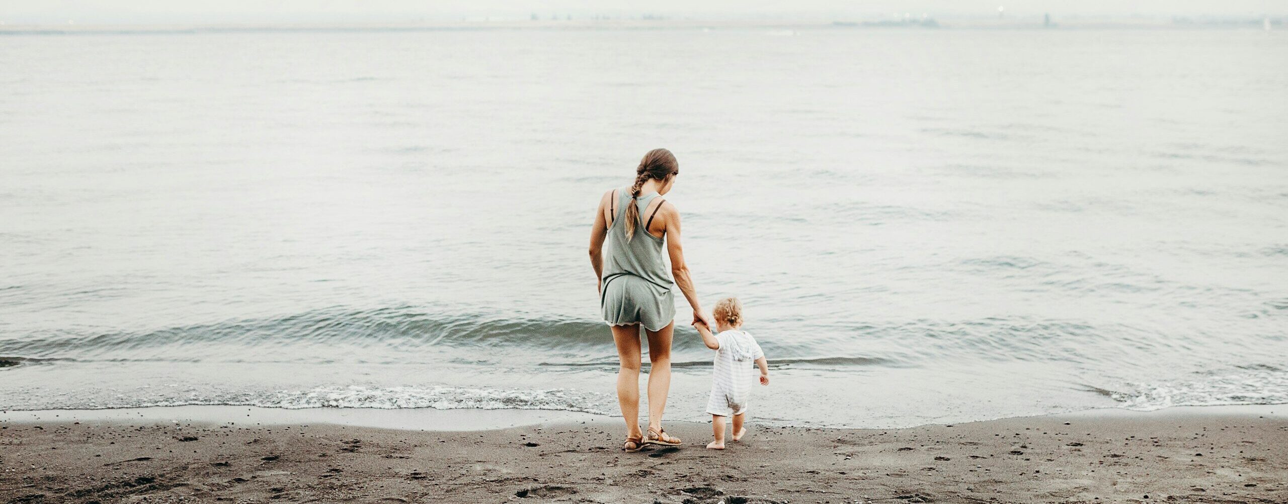 woman and baby walking on gray sand seashore during daytime