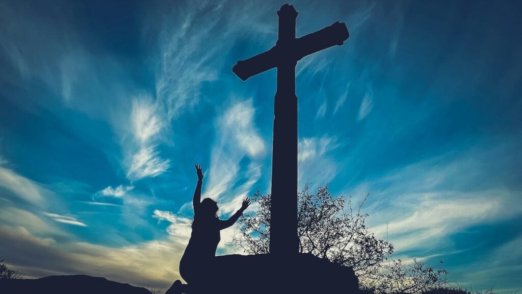 a person reaching up to a cross on a hill