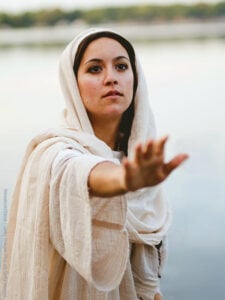 A shallow focus shot of a female wearing a biblical robe while reaching towards the hand of Jesus Christ