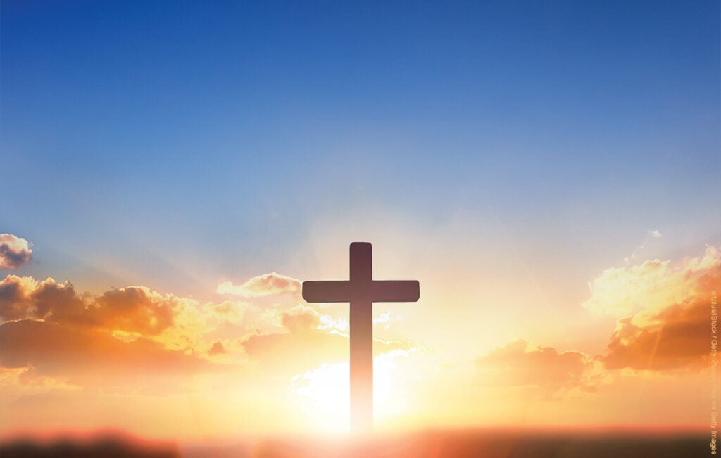 Silhouettes of crucifix symbol on top mountain with bright sunbeam on the colorful sky background