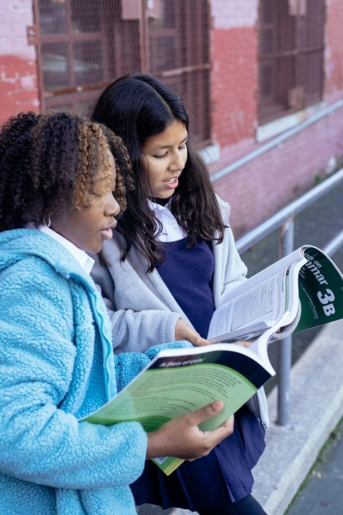 Side view of clever multiracial pupils speaking and reading textbooks while standing near school