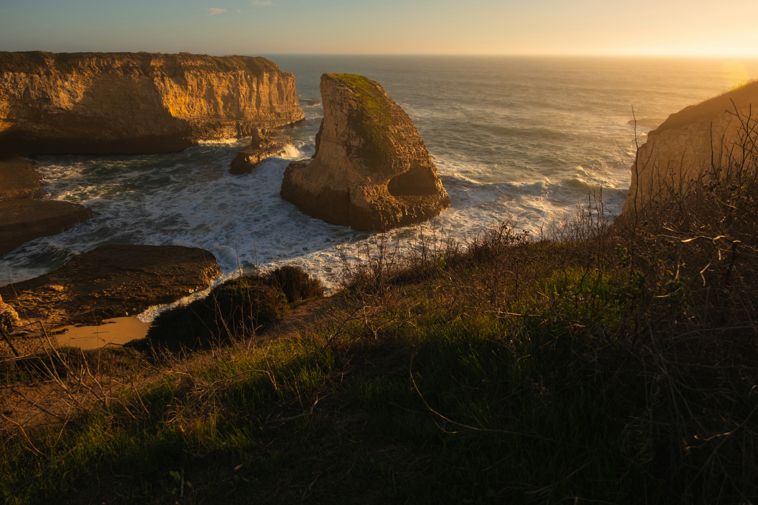 Golden hour illuminates rocky coastline with crashing waves