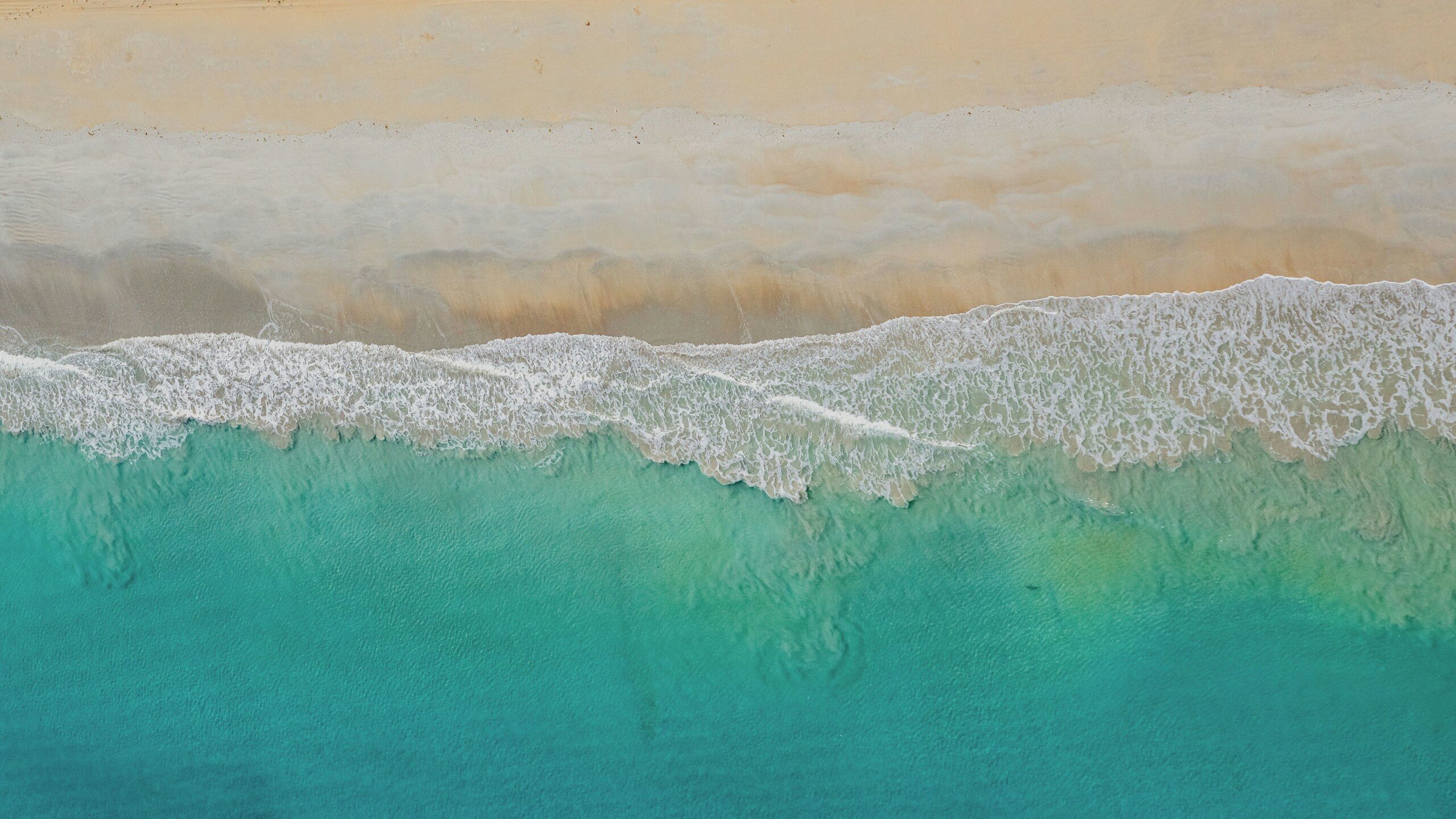 Turquoise ocean waves gently crash on a sandy beach.