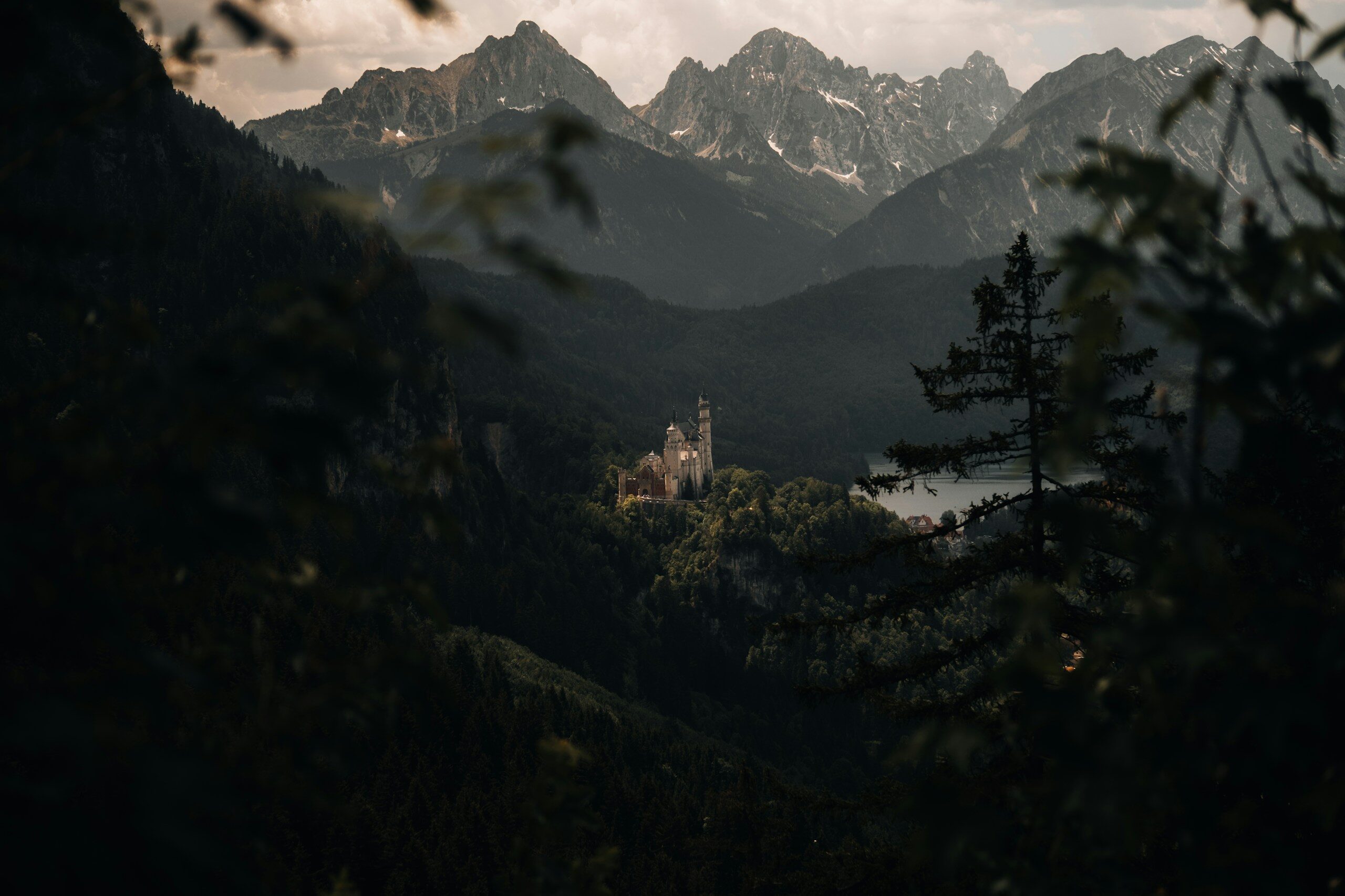 Castle in a valley framed by trees with mountains behind.