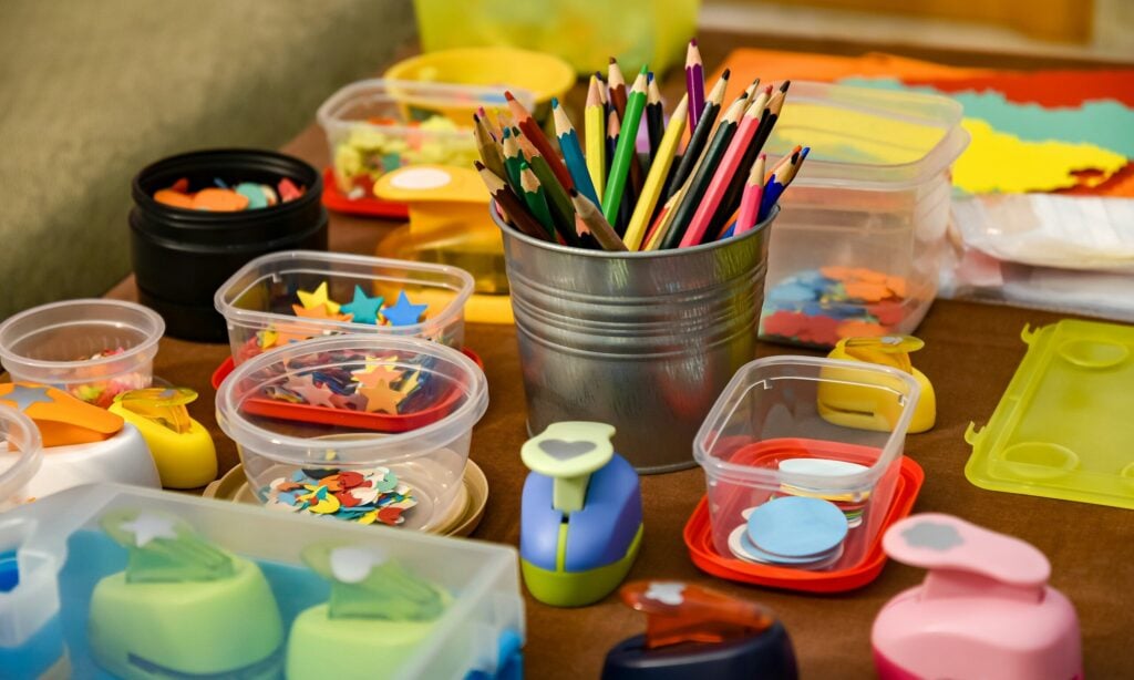 Colored pencils in a metal cup surrounded by plastic containers of paper shapes