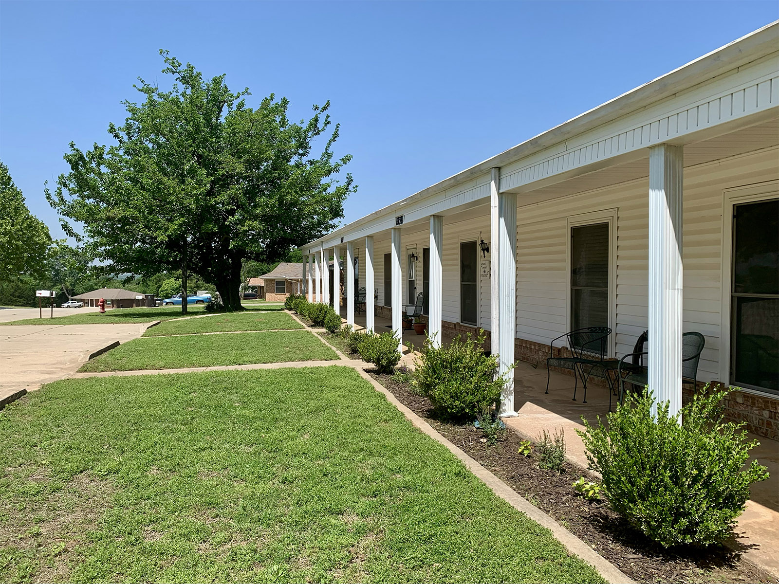 Summit Ridge apartment building with shaded porch, landscaping, and large tree at the end of the walkway