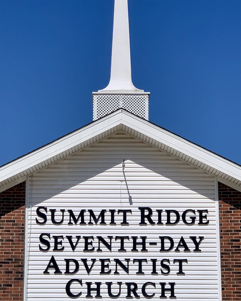 Welcome sign and white church steeple of the Summit Ridge SDA Church beneath a clear blue sky