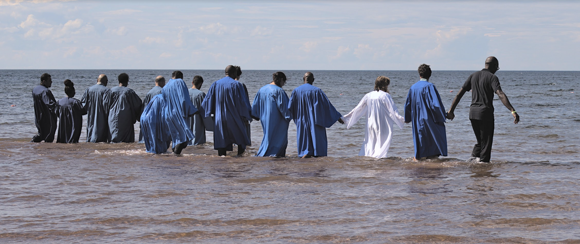 A group of people in robes walking into the water for baptism at Camp Pugwash.