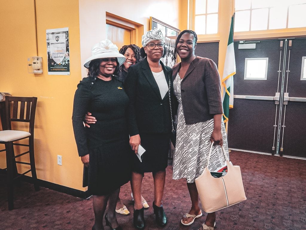 A group of women in church dresses and hats smiling together at a church gathering
