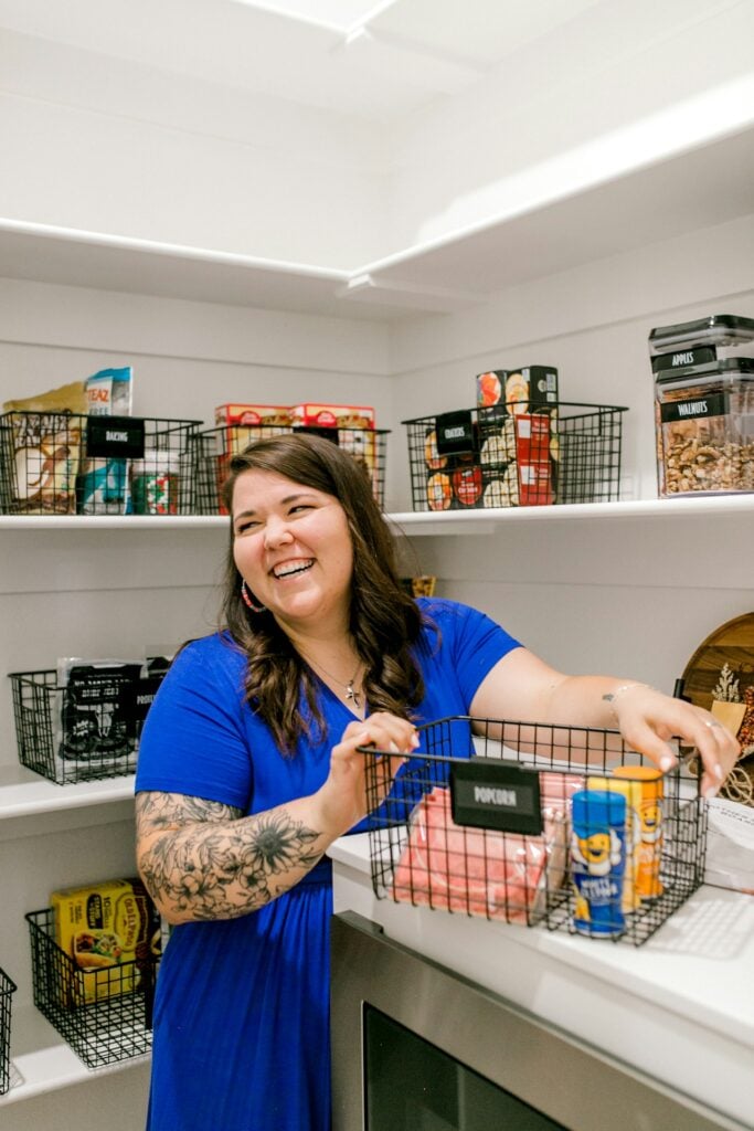 Woman organizing pantry with organized shelves and labeled shelves.