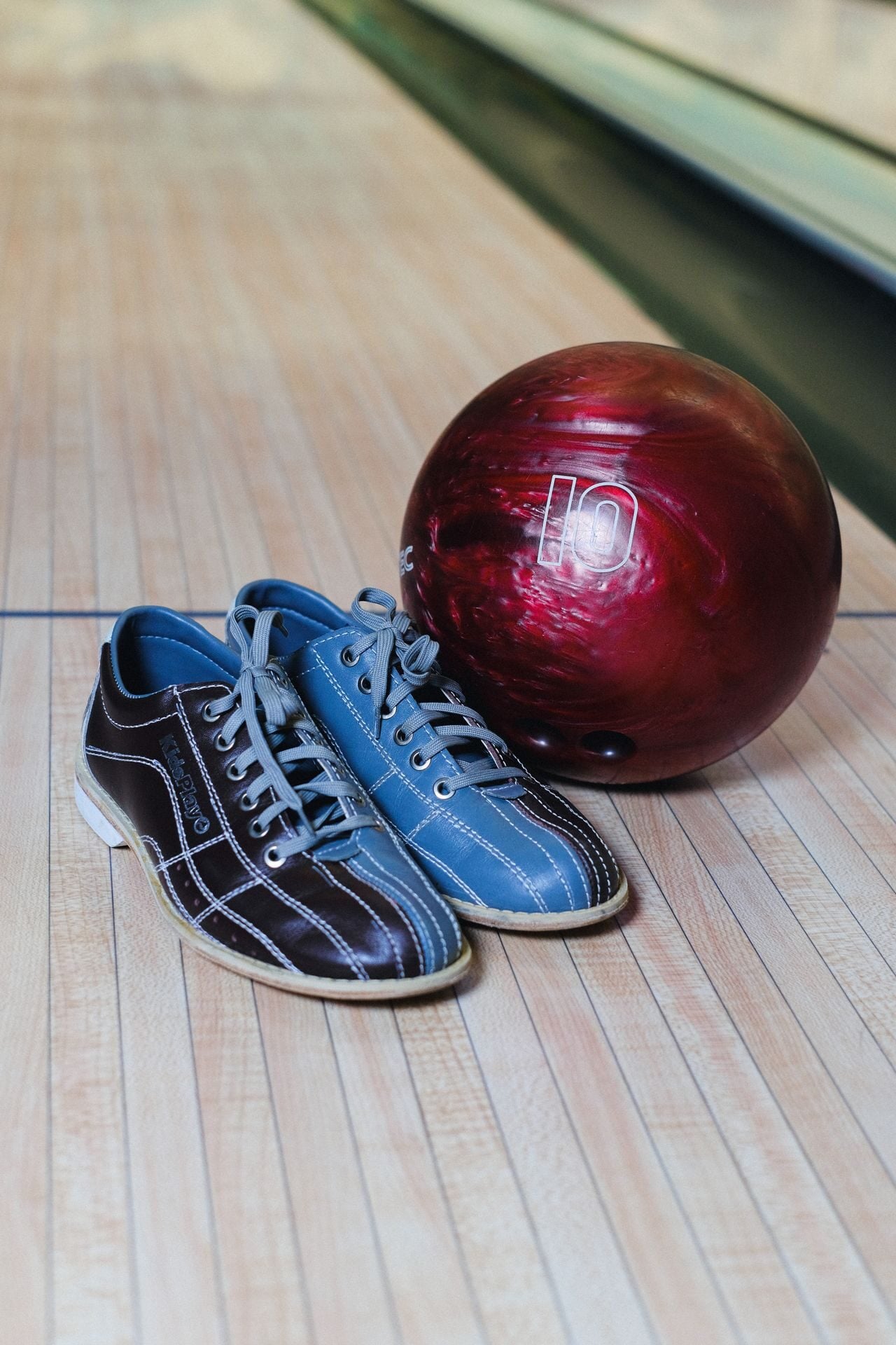 A pair of colorful bowling shoes beside a maroon bowling ball on a wooden lane.