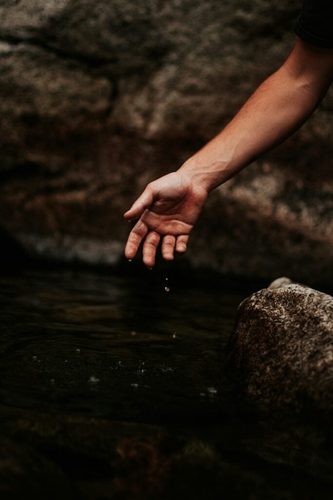 a person's hand touching a rock in the water