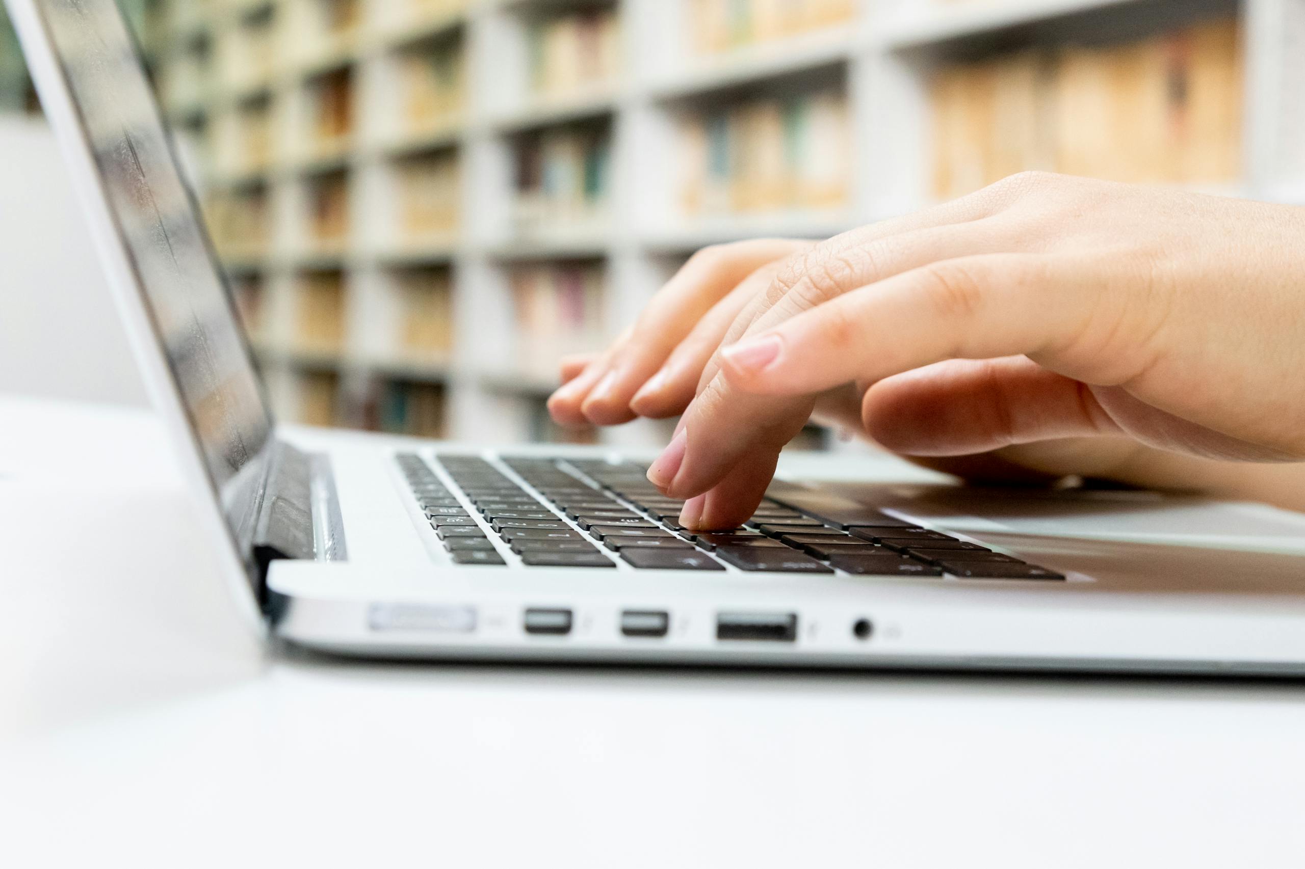 Close-up of hands typing on a laptop keyboard in a library setting.