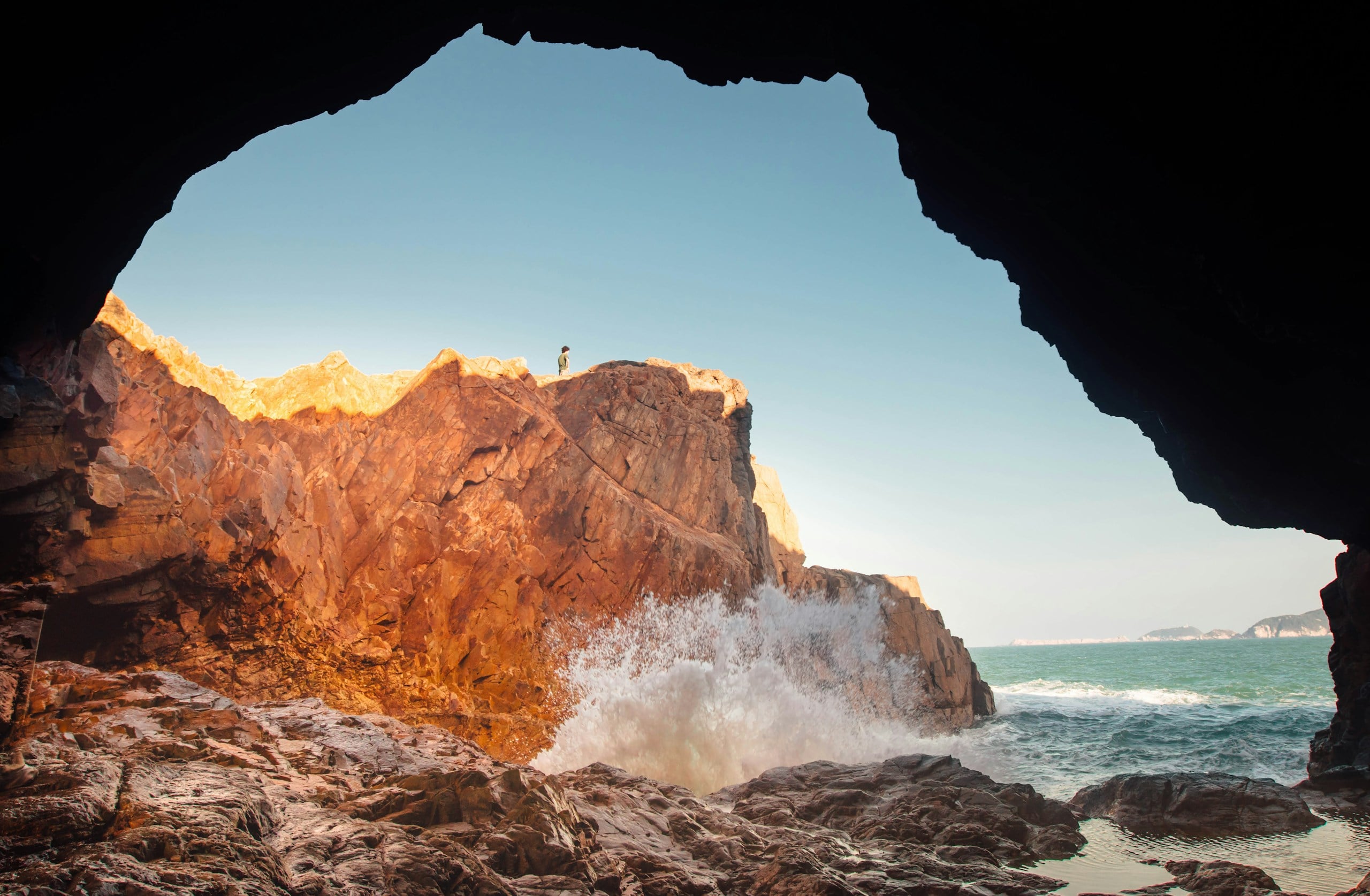 Waves crashing against rocky cliffs under a clear sky.